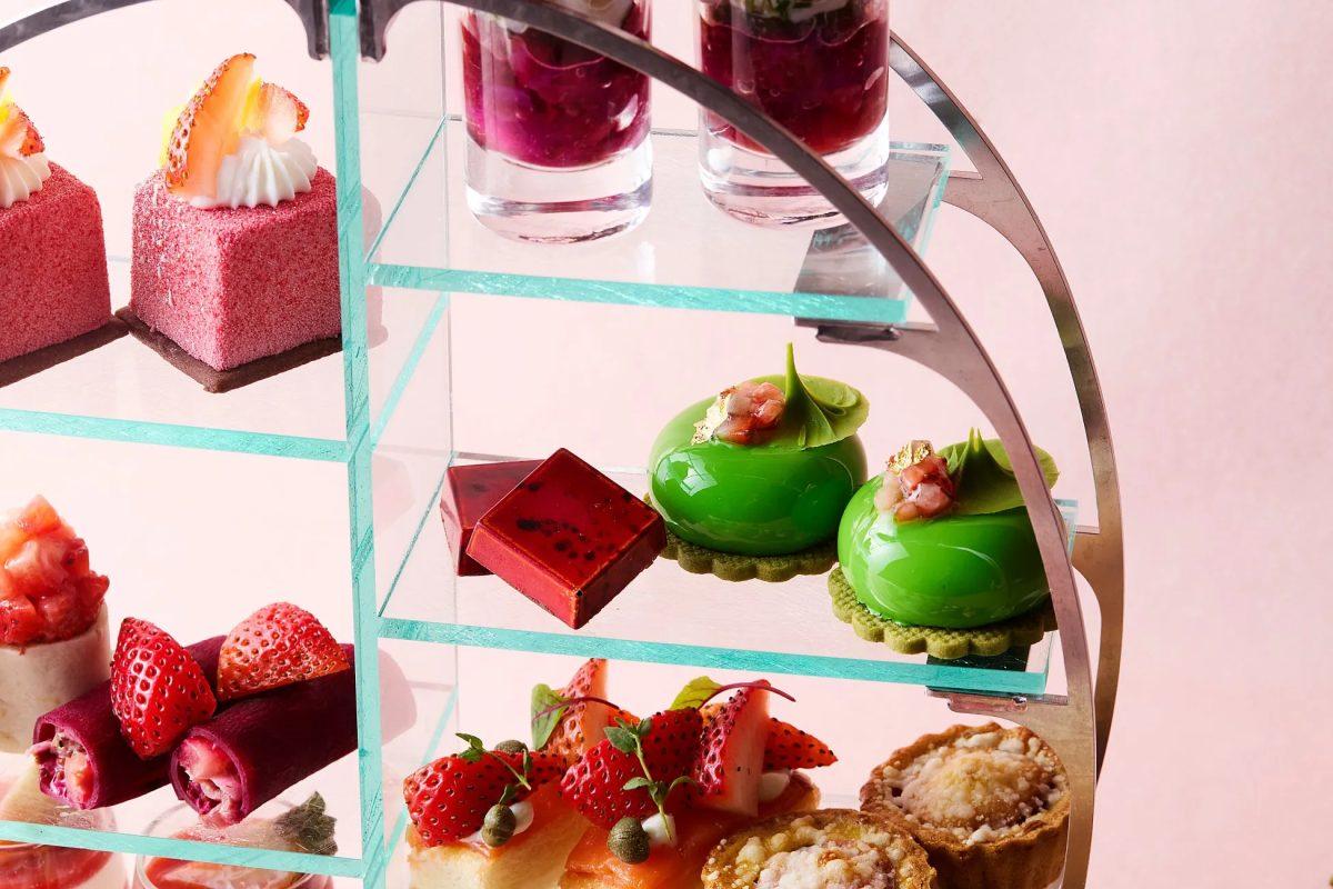 アフタヌーンティーのセット。様々な種類のスイーツがガラスの棚に並べられている。上段にはイチゴとクリームが乗ったケーキ、2段目には緑色のムース、3段目にはイチゴと野菜を巻いたものやタルト。