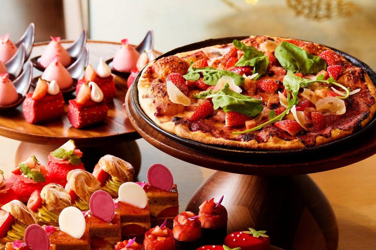 デザートが並べられた写真。ピザ、ケーキ、ムースなど様々な種類のデザートが木製の台に美しく配置されている。