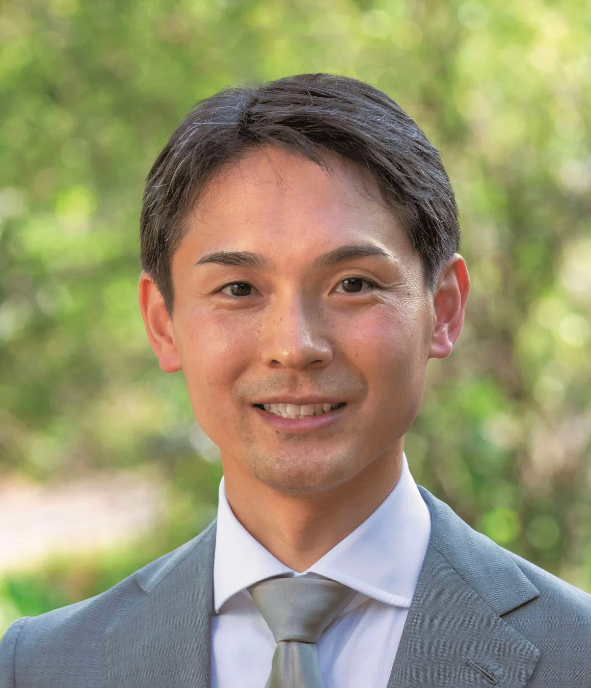 笑顔の男性のポートレート。彼はグレーのスーツと白いシャツ、ネクタイを着ています。背景はぼやけています。