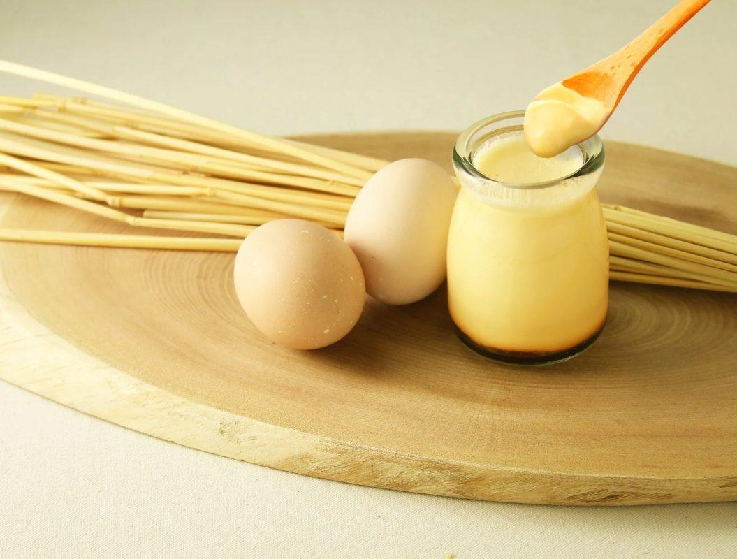 プリンが入ったガラス瓶、卵2個、木のスプーンが置かれている写真