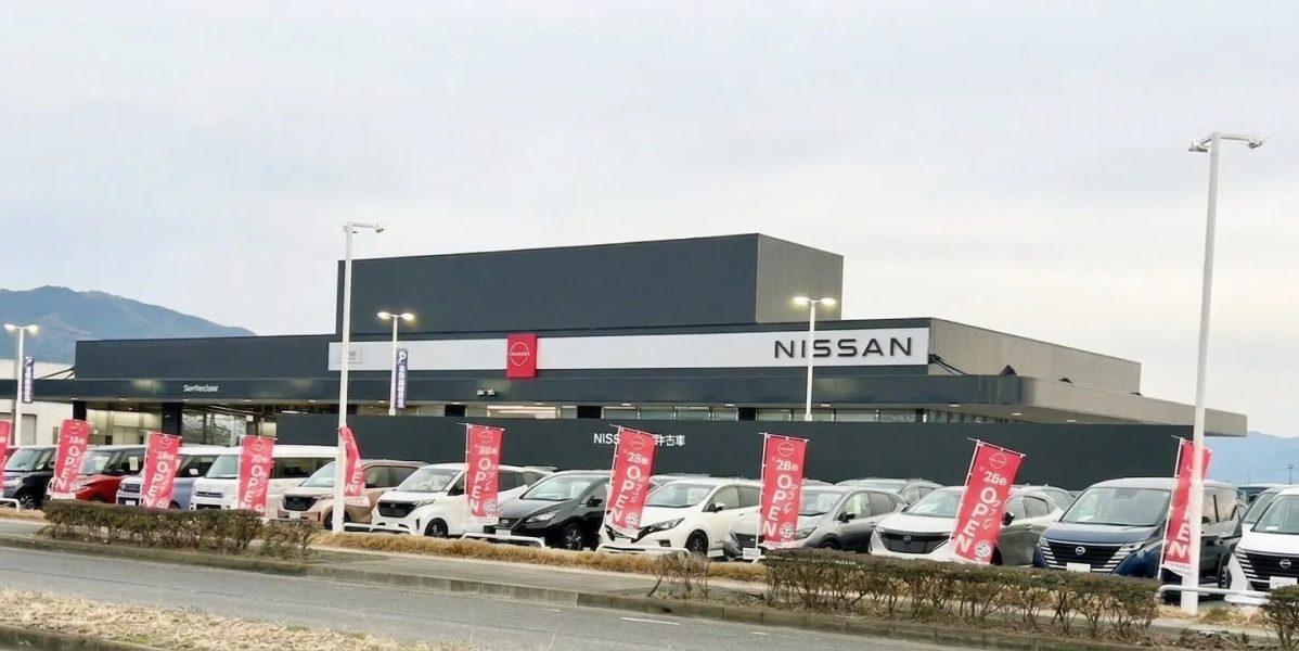 日産の販売店の写真。多くの車が展示されており、オープンと書かれた旗が立っている。