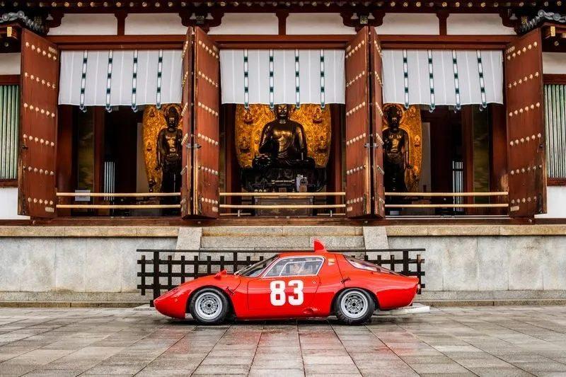 お寺の前に赤いレーシングカーが停まっている写真です